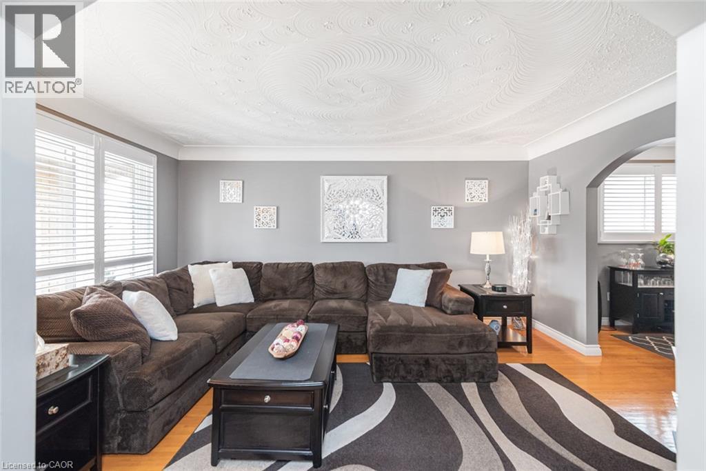 Living area featuring wood-finish flooring, bay windows with blinds, an arched doorway, and crown molding - 366 Berkindale Drive, Hamilton, ON