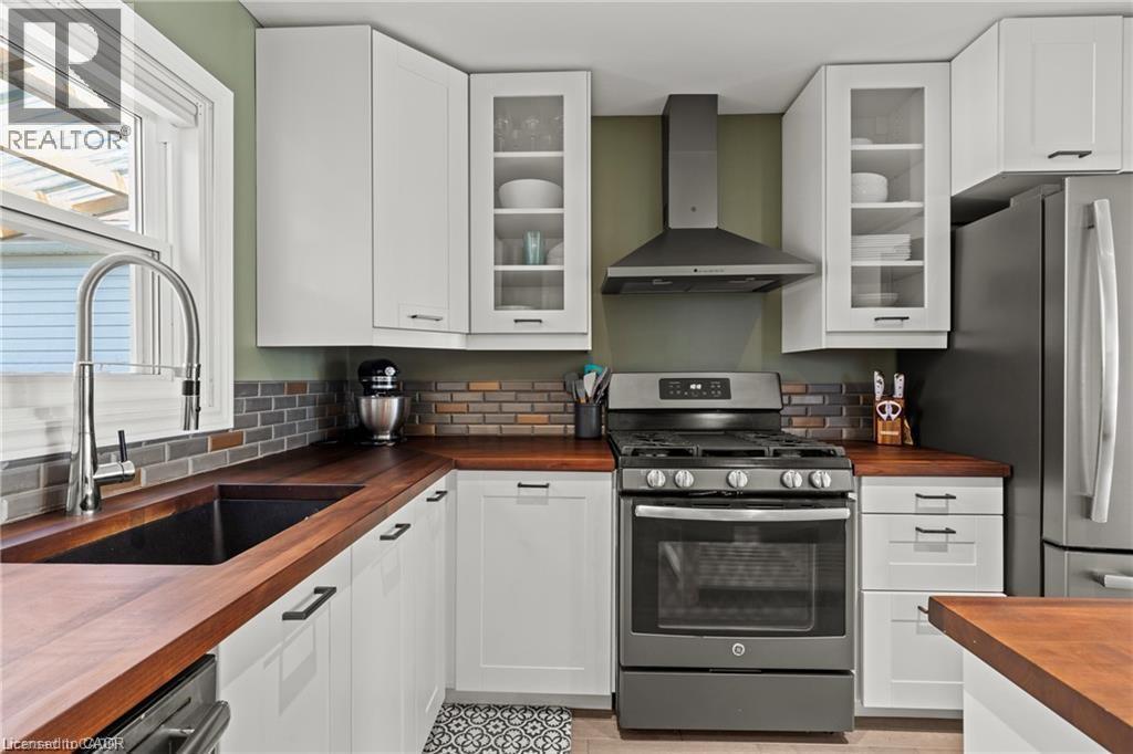Modern kitchen featuring white cabinetry, wood-finish countertops, and a gray subway tile backsplash - 33 Huxley Avenue N, Hamilton, ON
