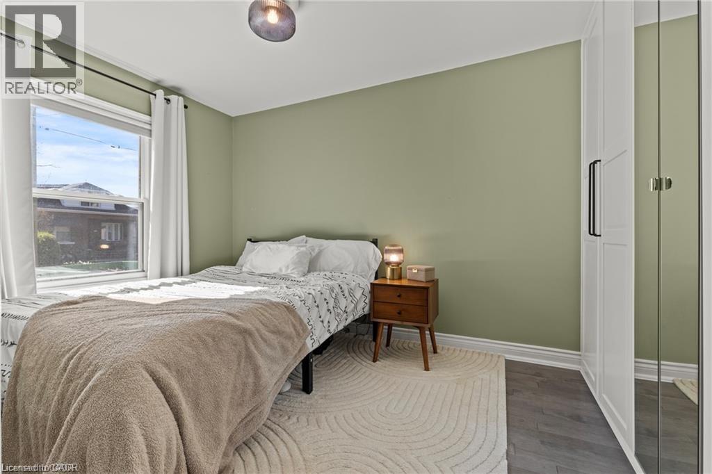 Bright room featuring a large window, light green painted walls, dark wood-finish flooring, and white trim - 33 Huxley Avenue N, Hamilton, ON