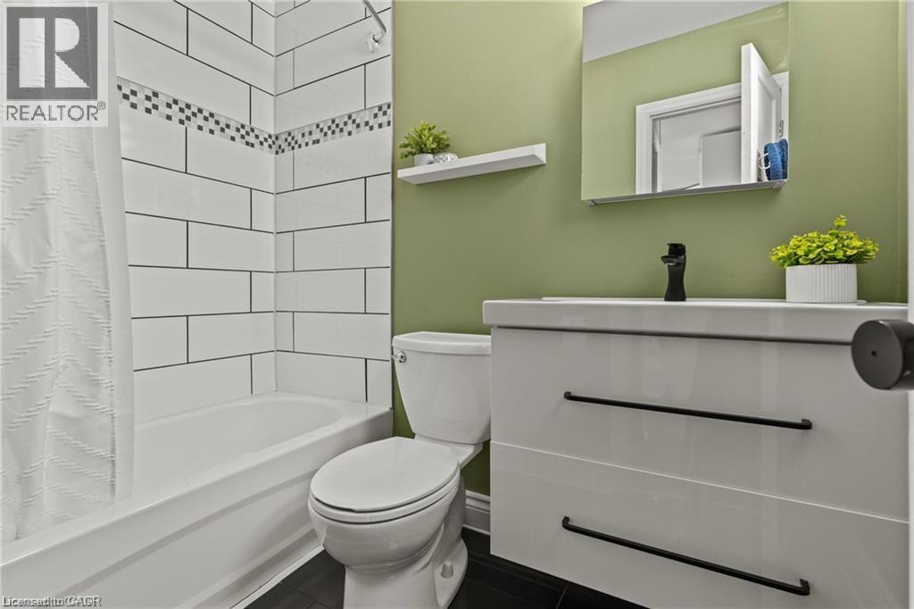 Bathroom featuring a white subway tile shower surround with a decorative accent band, a white bathtub, and dark flooring - 33 Huxley Avenue N, Hamilton, ON