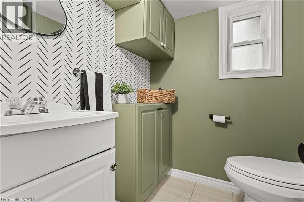 Bathroom featuring a white vanity with integrated sink, chrome faucet, and patterned accent wall - 33 Huxley Avenue N, Hamilton, ON