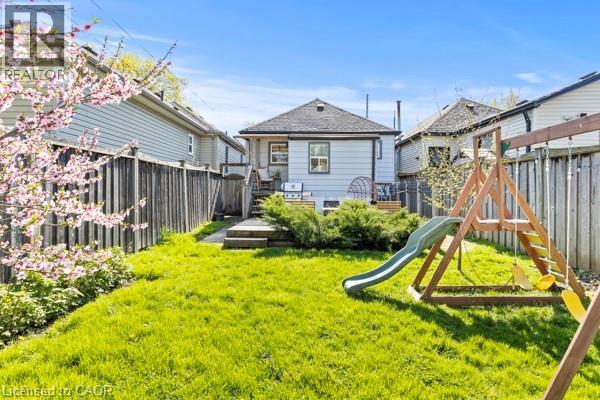 Expansive green lawn with a privacy fence, mature flowering tree, and an elevated wood deck with steps - 33 Huxley Avenue N, Hamilton, ON