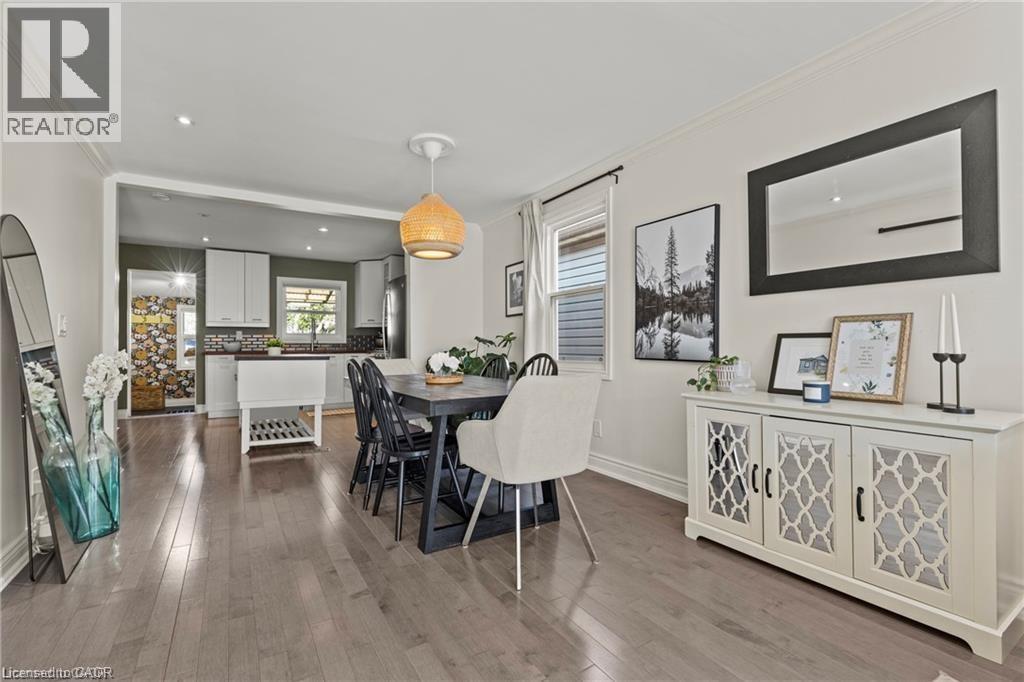 Spacious dining area featuring wood-finish flooring, a contemporary ceiling fixture, and a built-in white buffet cabinet with decorative glass panels - 33 Huxley Avenue N, Hamilton, ON