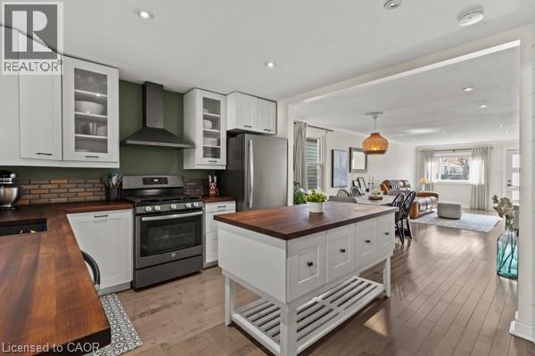Open-concept kitchen featuring white cabinetry, wood-finish countertops, stainless steel appliances, and a central island with storage - 33 Huxley Avenue N, Hamilton, ON