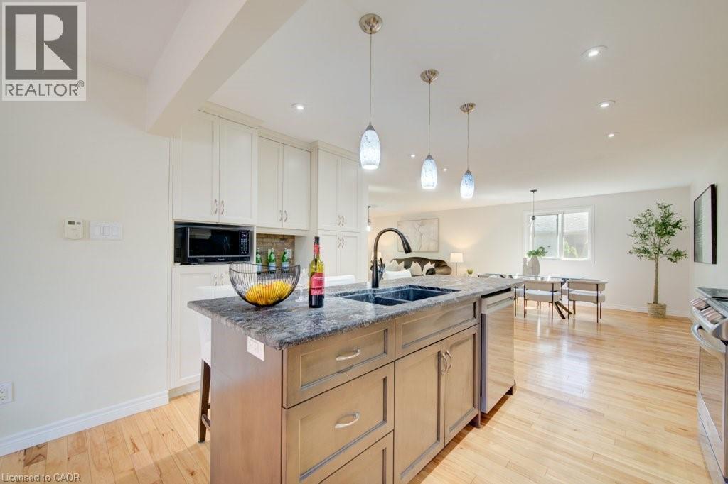 Kitchen island featuring a dark countertop, undermount sink with a gooseneck faucet, and integrated dishwasher - 60 Mayfield Avenue, Waterloo, ON