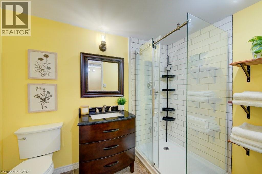 Bathroom featuring a glass-enclosed shower with subway tile surround, dark wood-finish vanity with an undermount sink, and wood-finish flooring - 60 Mayfield Avenue, Waterloo, ON