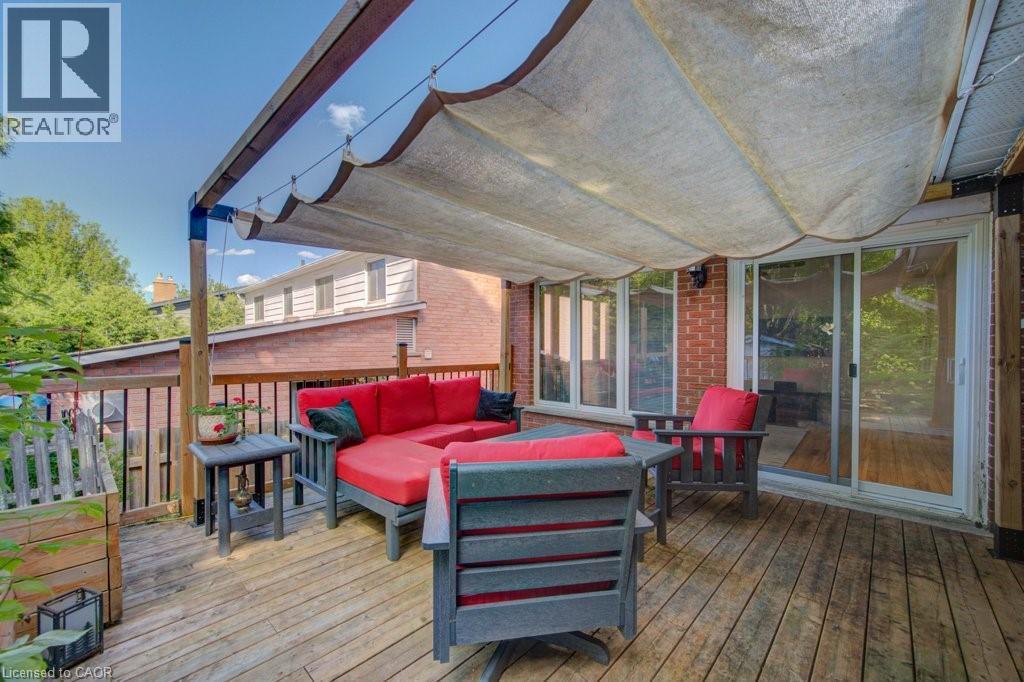 Expansive wood-finish deck featuring a retractable fabric awning, full-height sliding glass doors, brick exterior, and wood railing - 60 Mayfield Avenue, Waterloo, ON