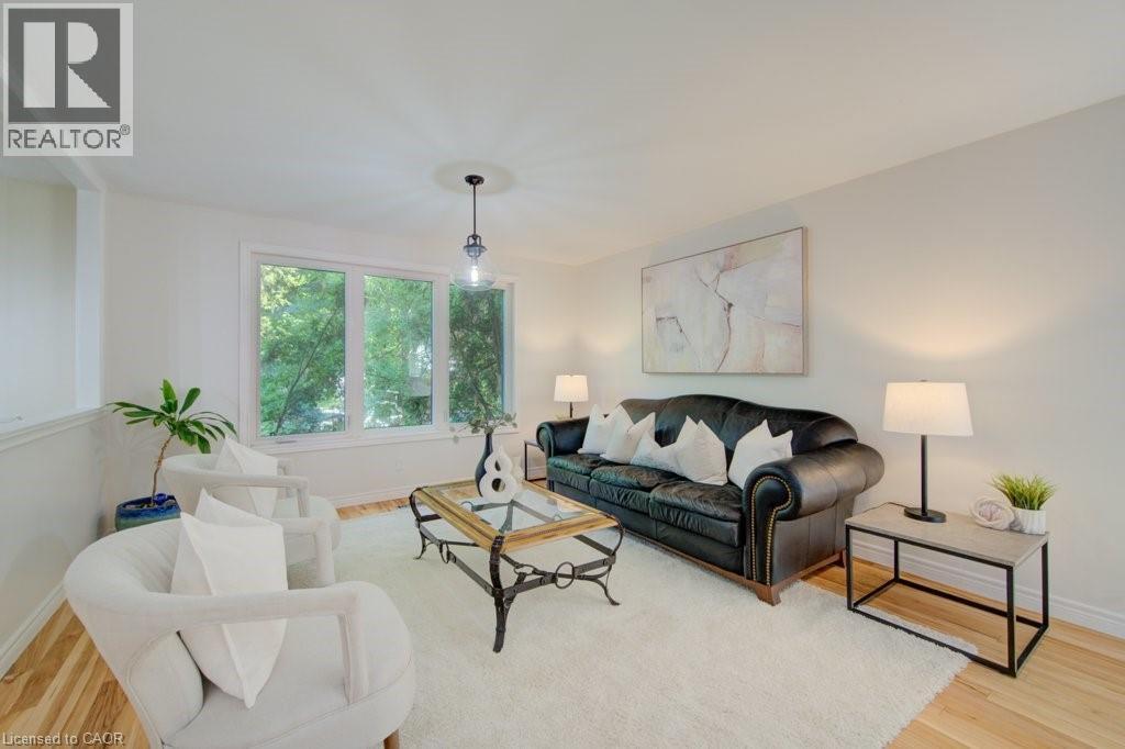 Bright living area featuring wood-finish flooring, a large multi-pane window, and a ceiling-mounted pendant light fixture with a decorative medallion - 60 Mayfield Avenue, Waterloo, ON
