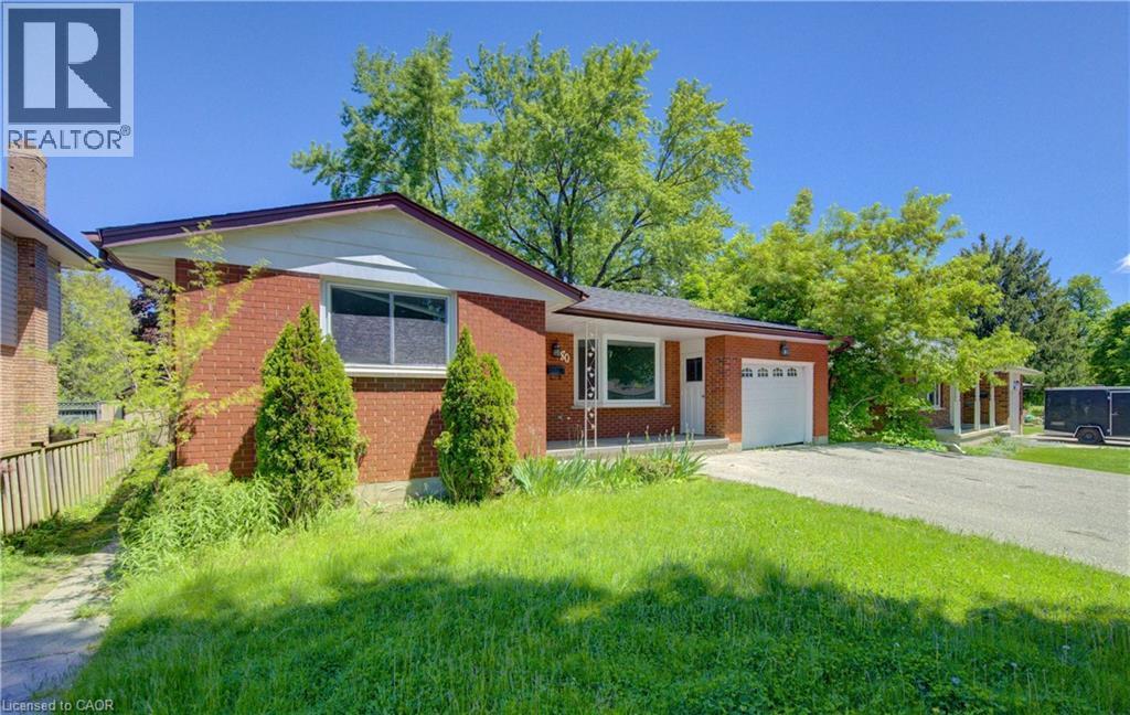 Red brick exterior home featuring a single garage door, a concrete driveway, a front lawn, and mature trees - 80 Lower Canada Crescent, Kitchener, ON