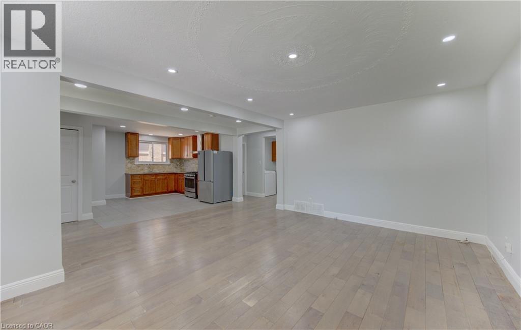 Spacious living area featuring light wood-finish flooring, recessed lighting, and crisp white walls, opening to a kitchen with wood cabinetry and stainless steel appliances - 80 Lower Canada Crescent, Kitchener, ON