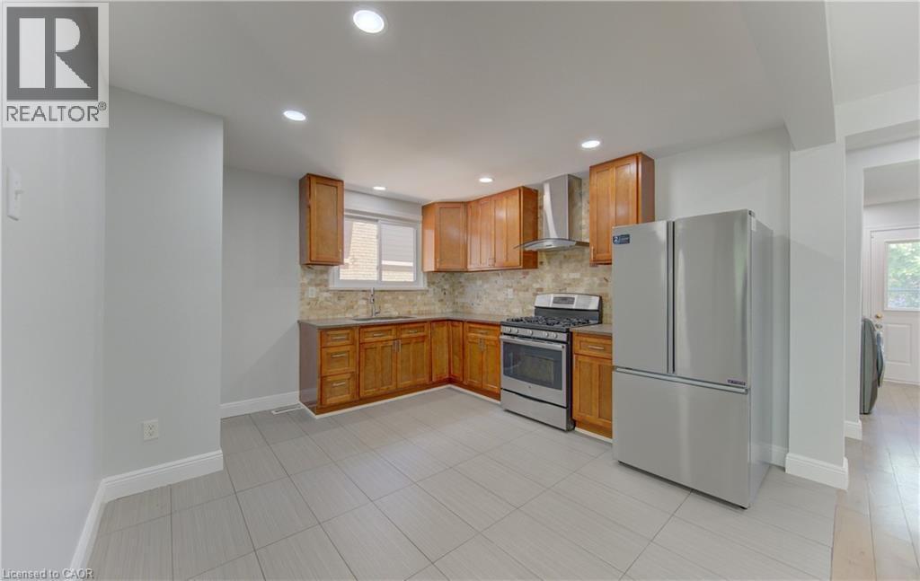 Kitchen featuring light wood cabinetry, stone-look backsplash, and stainless steel appliances - 80 Lower Canada Crescent, Kitchener, ON