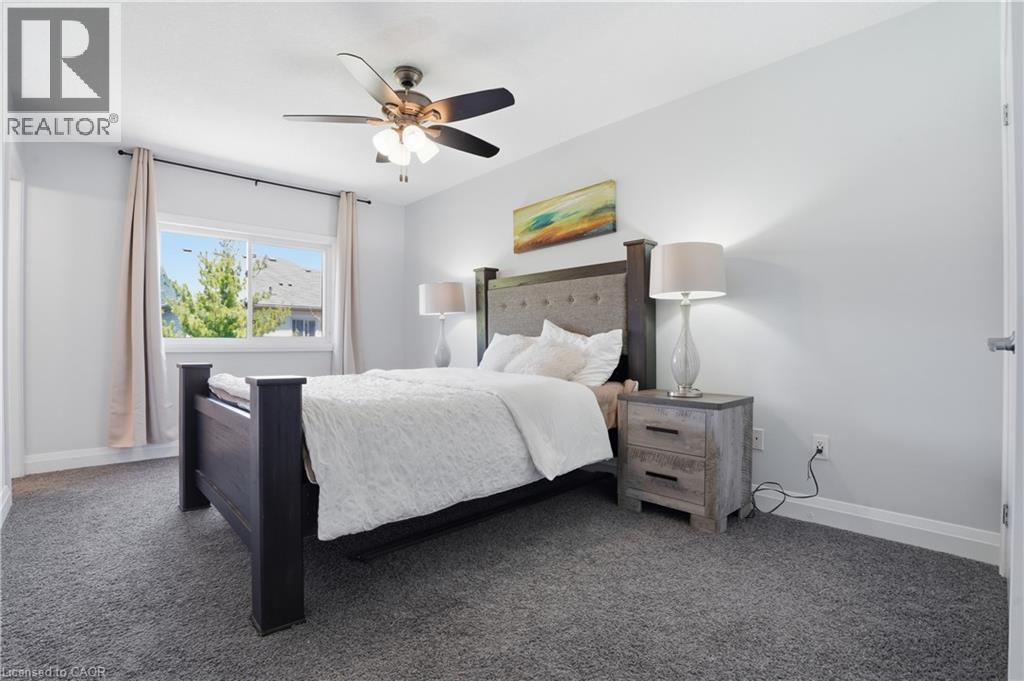 Primary Bedroom featuring plush grey carpeting, a multi-pane window with a light-colored frame, a ceiling fan with integrated lighting, and light-toned wall finishes - 7 Upper Mercer Street Unit# G30, Kitchener, ON - Indoor Photo Showing Bedroom