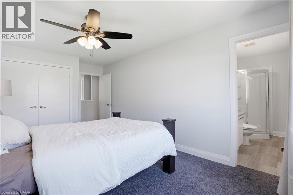 Bedroom featuring light gray walls, dark blue carpeting, a ceiling fan with integrated lighting, a double-door closet, and an entry to a bathroom with wood-finish flooring and a shower enclosure - 7 Upper Mercer Street Unit# G30, Kitchener, ON - Indoor Photo Showing Bedroom