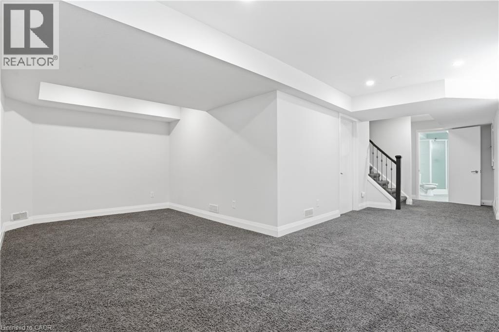 Spacious lower-level area featuring gray carpeting, white walls, recessed lighting, a staircase with dark banister, and a full bathroom with glass-enclosed shower - 7 Upper Mercer Street Unit# G30, Kitchener, ON - Indoor Photo Showing Other Room