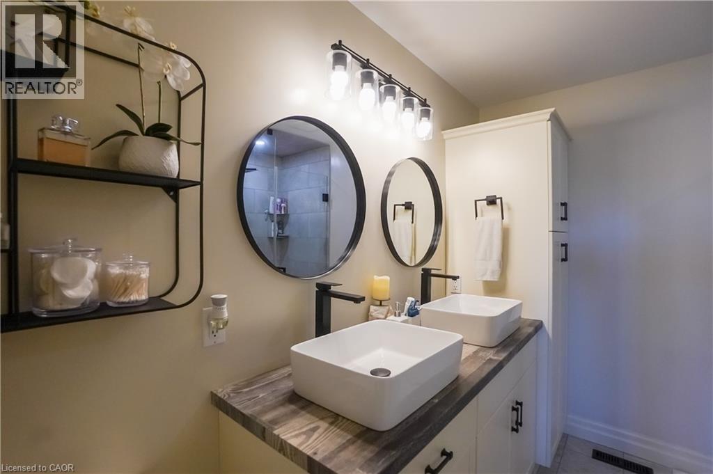 Bathroom vanity featuring dual vessel sinks, black hardware, wood-finish countertop, and integrated storage cabinetry - 365 Poldon Drive, Norwich, ON