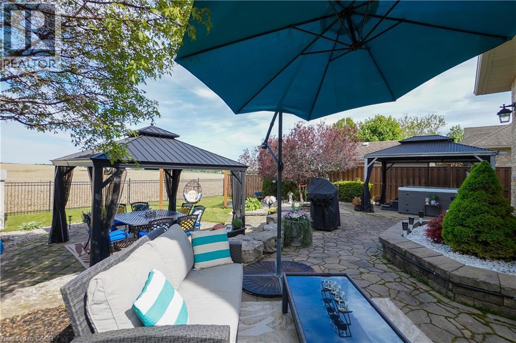 Expansive stone paver patio featuring a covered gazebo, raised garden beds, and mature landscaping - 365 Poldon Drive, Norwich, ON