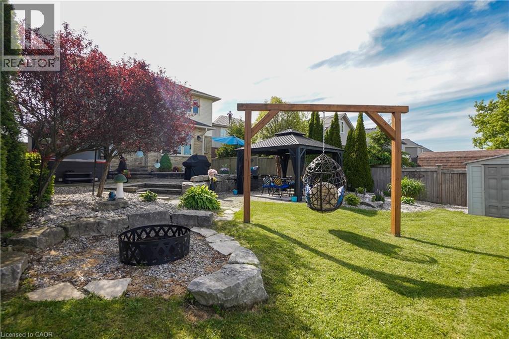Expansive backyard featuring a lush lawn, a stone-edged fire pit area, and a tiered patio with a covered gazebo - 365 Poldon Drive, Norwich, ON