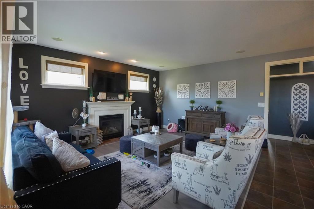 Living area featuring a white mantel fireplace, recessed lighting, two windows with blinds, wood-finish flooring, and a decorative doorway with an arched transom - 365 Poldon Drive, Norwich, ON