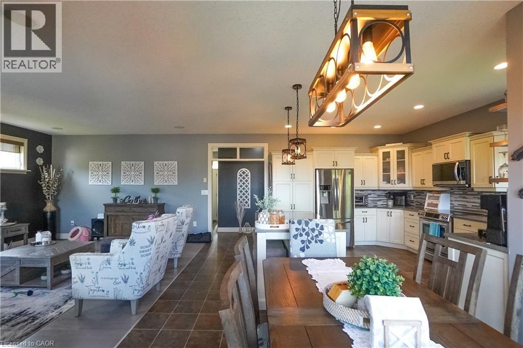 Open-concept living space featuring a spacious kitchen with cream cabinetry and stainless steel appliances, a dining area with a wood-finish table, and a living area with a dark accent wall - 365 Poldon Drive, Norwich, ON
