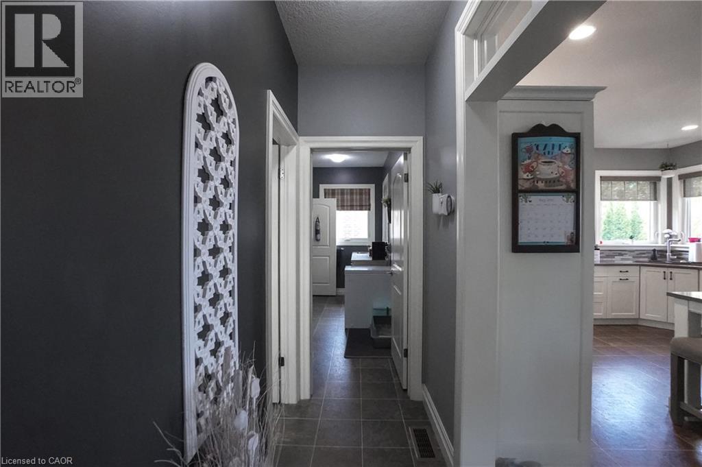 Hallway featuring dark gray walls, white trim, and tile flooring, opening to a kitchen with light cabinetry and wood-finish flooring - 365 Poldon Drive, Norwich, ON