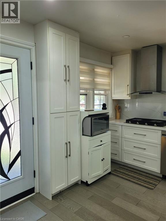 Kitchen featuring white shaker-style cabinetry, stainless steel range hood, stone countertops, and a white tile backsplash - 153 Arnold Street, Kitchener, ON