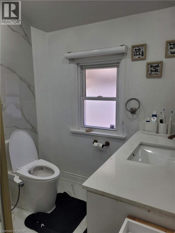 Bathroom featuring a white vanity with an integrated sink, a built-in toilet, white marble-look wall tiling, and white wood-finish window trim - 153 Arnold Street, Kitchener, ON