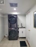 Laundry area featuring stacked appliances, a utility sink with a tall faucet, white base cabinetry, and neutral tile flooring -