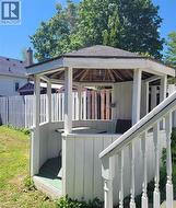 Hexagonal gazebo with shingle roof and white paneling, featuring a built-in light fixture and a wooden floor -