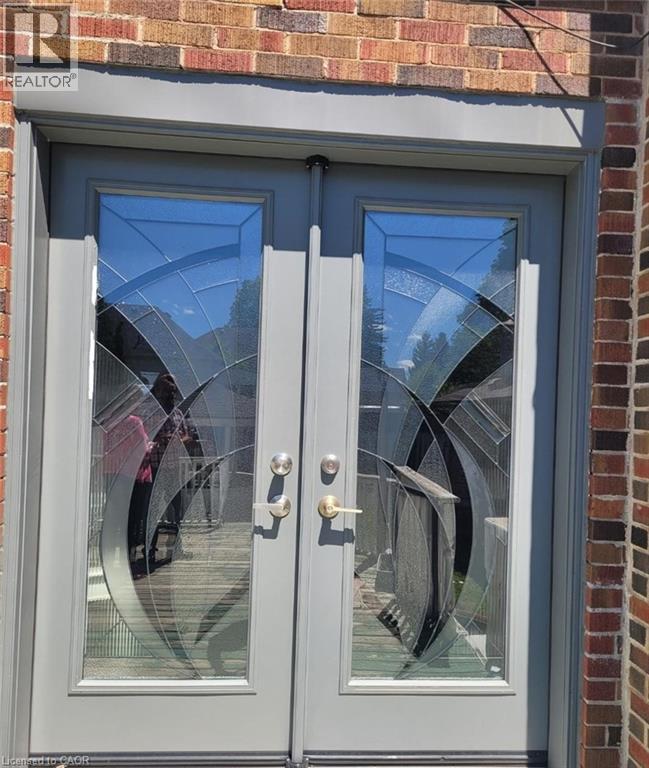 Double doors featuring decorative glass inserts and brushed metal hardware, set against a brick exterior - 153 Arnold Street, Kitchener, ON