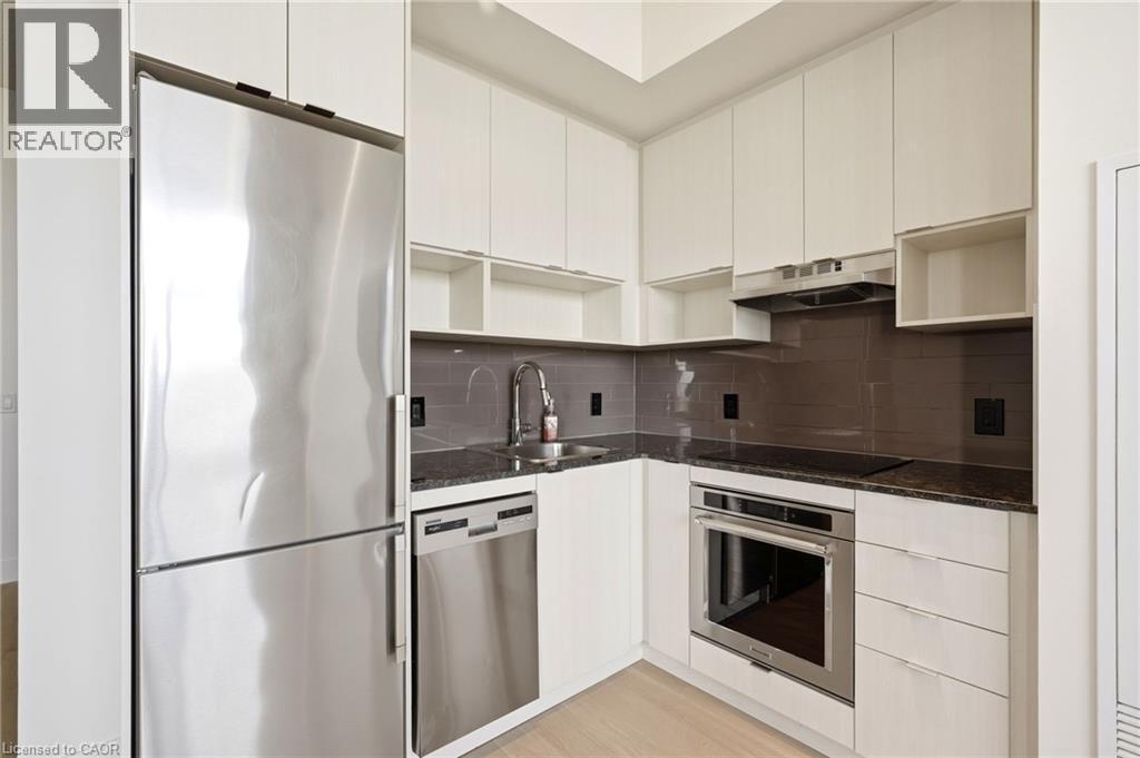 Modern kitchen featuring stainless steel appliances, dark stone countertops, a tile backsplash, light wood-finish flooring, and white cabinetry - 7 Mabelle Avenue Unit# Ph07, Toronto, ON