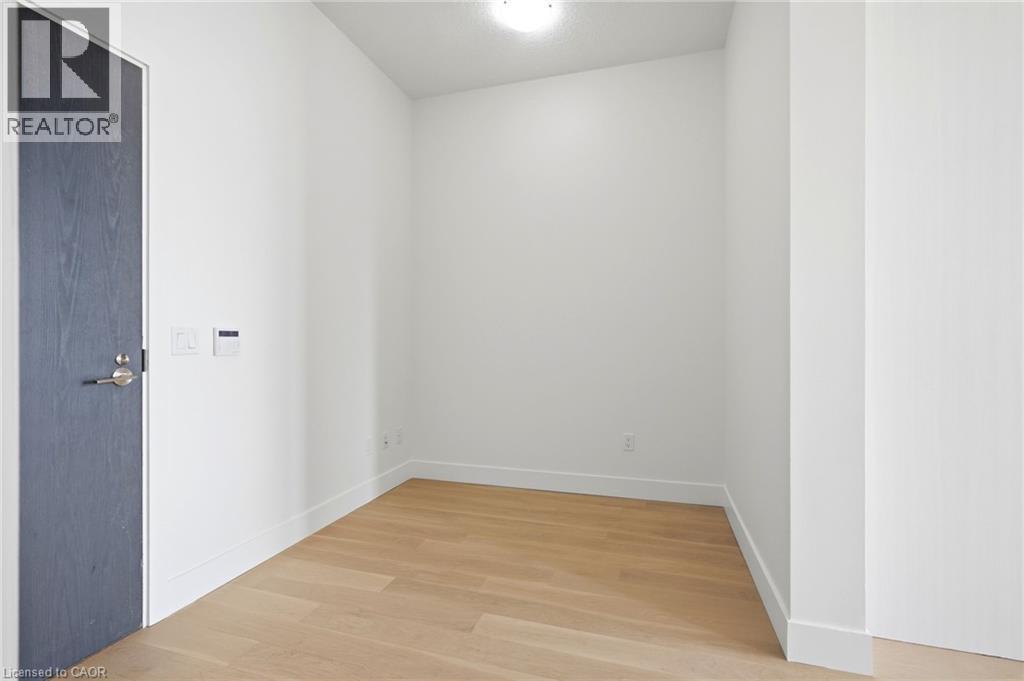Bright interior space featuring light wood-finish flooring, white baseboards, and a contemporary dark wood-grain door with brushed nickel hardware - 7 Mabelle Avenue Unit# Ph07, Toronto, ON