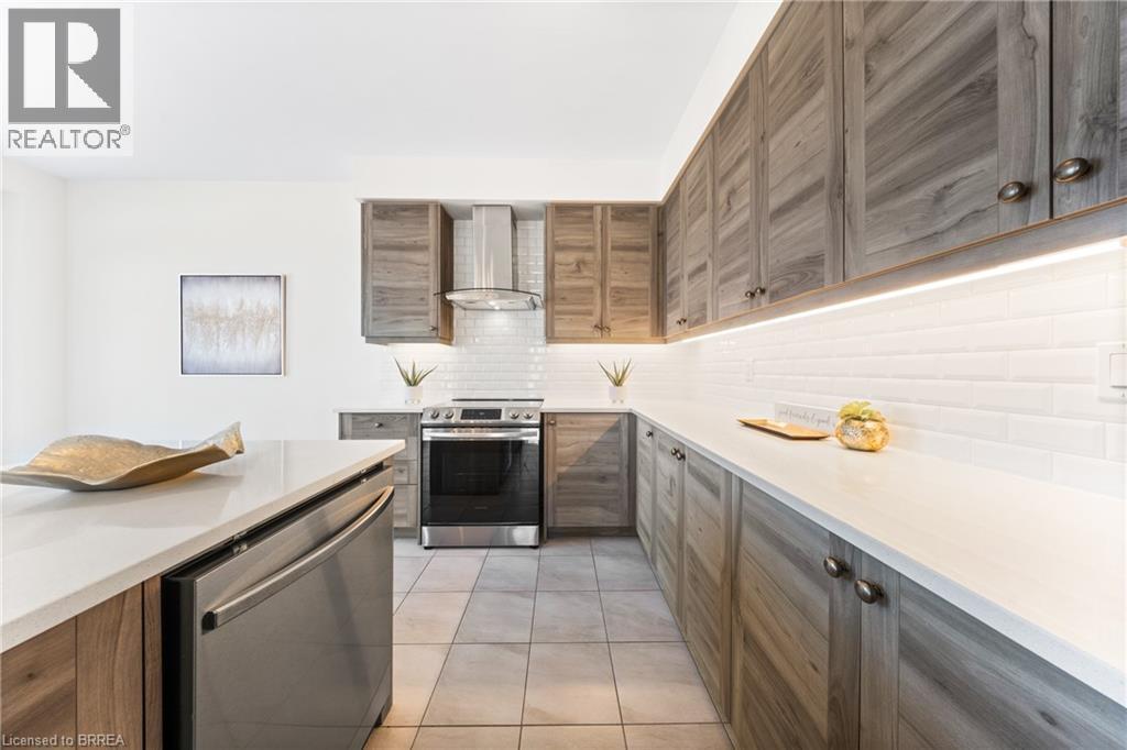 Kitchen featuring backsplash, appliances with stainless steel finishes, light tile patterned flooring, wall chimney exhaust hood, and light stone countertops - 1 Bee Crescent, Brantford, ON