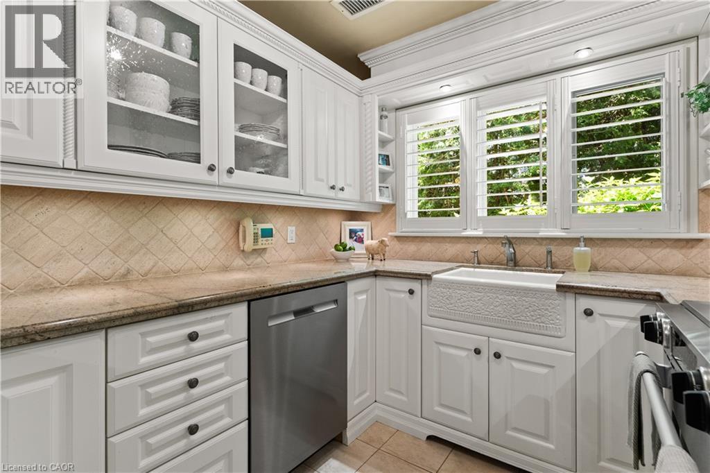 Kohler sink, tapsets, soap dispenser, hand spray. ""Seedy"" glass on cabinetry. Plantation shutters. Maytag dishwasher - 3040 First Street, Burlington, ON - Indoor Photo Showing Kitchen