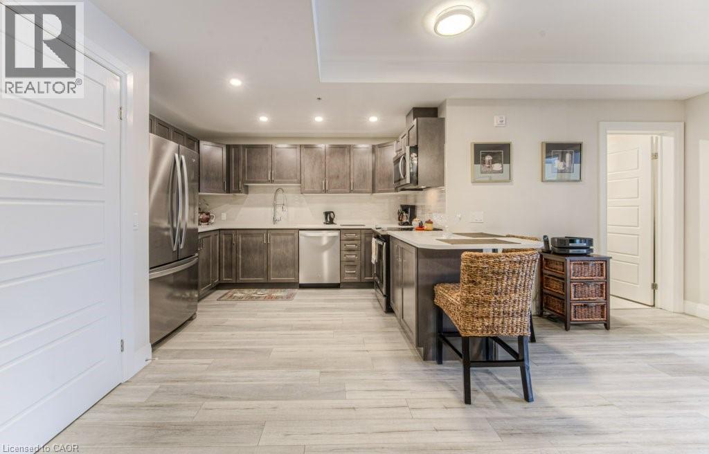 Kitchen featuring wood-finish flooring, stainless steel appliances, dark wood cabinetry, light countertops, and recessed lighting - 5 Wake Robin Drive Unit# 107, Kitchener, ON