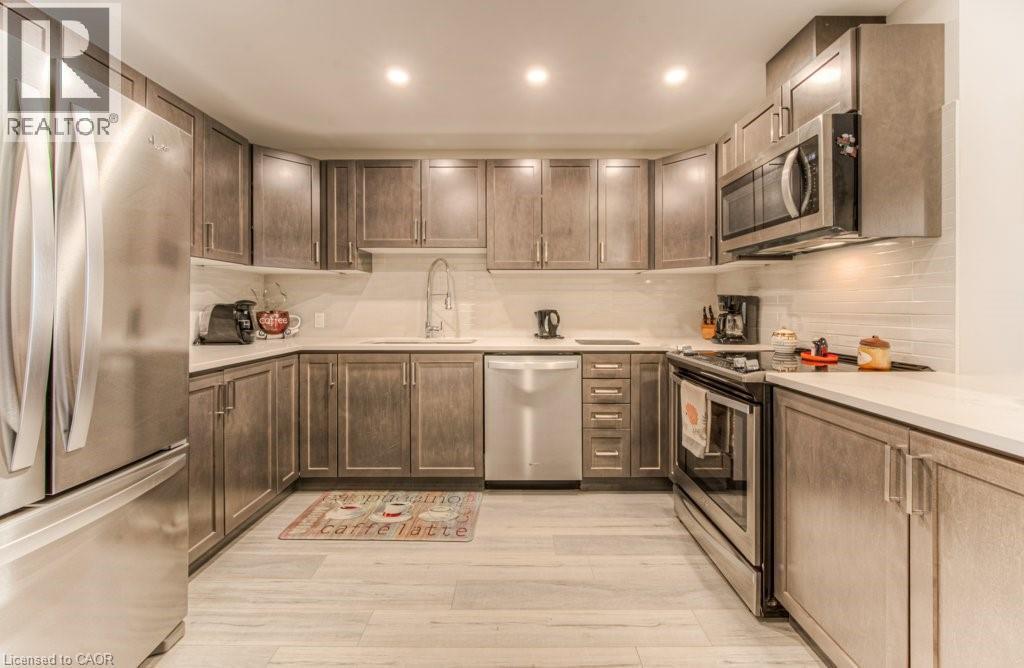 Kitchen featuring wood-finish cabinetry, stainless steel appliances, light-toned countertops, and a white subway tile backsplash - 5 Wake Robin Drive Unit# 107, Kitchener, ON