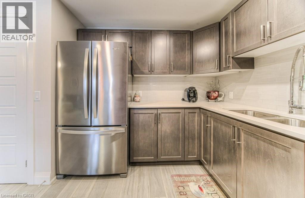 Kitchen featuring wood-finish cabinetry with modern pulls, stainless steel French door refrigerator, light-toned countertops, and a white subway tile backsplash - 5 Wake Robin Drive Unit# 107, Kitchener, ON