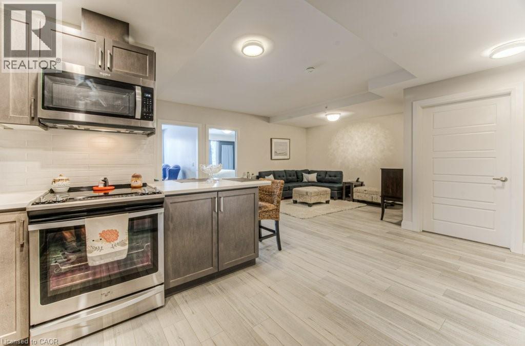 Modern kitchen featuring stainless steel appliances, wood-finish cabinetry, white tile backsplash, and light-toned countertops - 5 Wake Robin Drive Unit# 107, Kitchener, ON