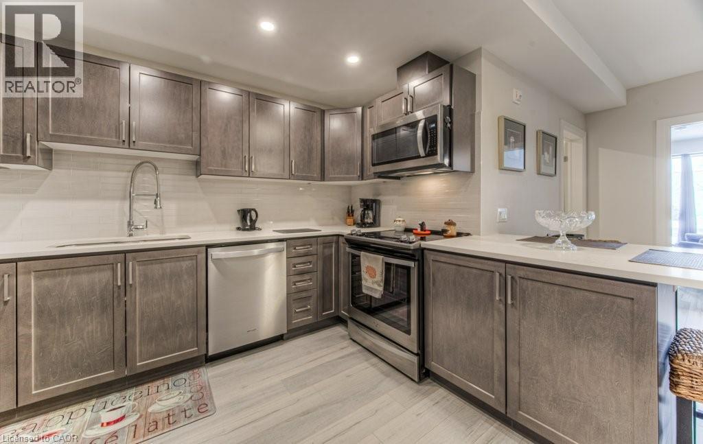 Contemporary kitchen featuring L-shaped cabinetry with stainless steel appliances, white countertops, and a white subway tile backsplash - 5 Wake Robin Drive Unit# 107, Kitchener, ON