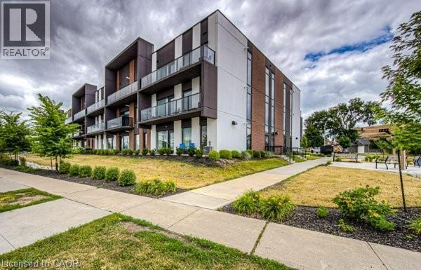 Contemporary multi-story building featuring a brick and panel facade, private balconies with glass railings, large windows, and a concrete sidewalk with landscaping - 5 Wake Robin Drive Unit# 107, Kitchener, ON