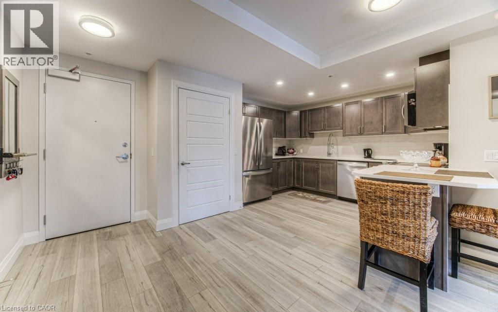 Open-concept kitchen and entry area featuring wood-finish flooring, contemporary flat-panel cabinetry, stainless steel appliances, and an eat-at counter - 5 Wake Robin Drive Unit# 107, Kitchener, ON