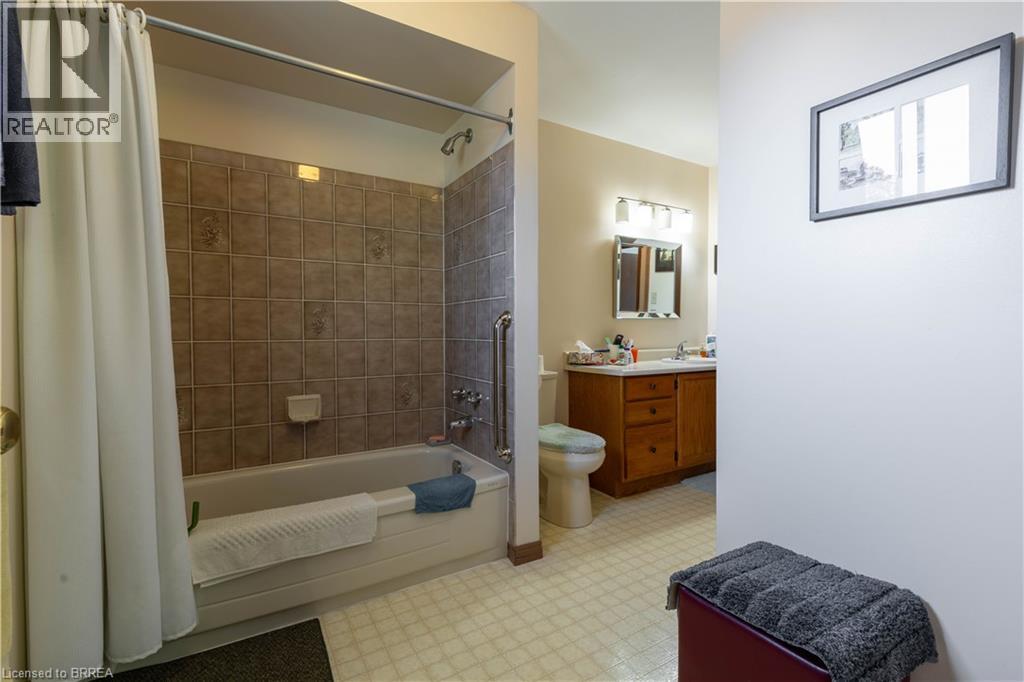 Bathroom featuring a tub/shower combination with tile surround, a built-in grab bar, and a single-sink vanity with wood-finish cabinetry - 12 Spartan Drive, Brantford, ON - Indoor Photo Showing Bathroom