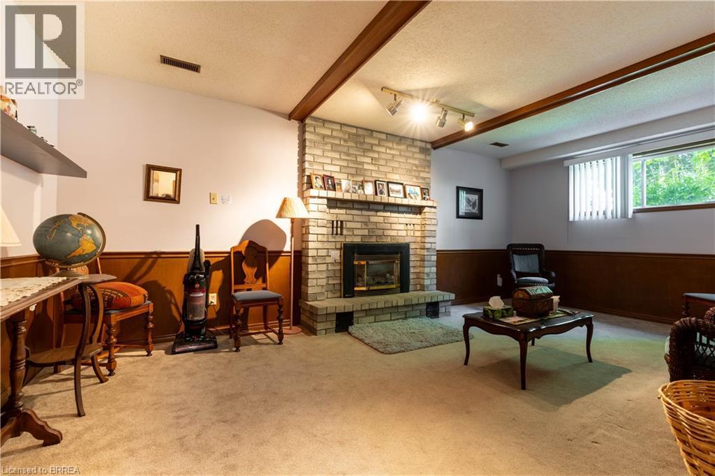 Spacious room featuring a brick fireplace with a raised hearth, wood-paneled wainscoting, track lighting, and a large window with blinds - 12 Spartan Drive, Brantford, ON - Indoor With Fireplace