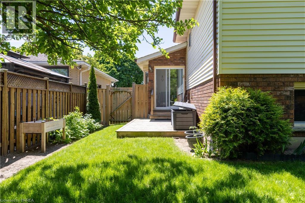 Expansive grassy yard featuring a wood fence, wooden gate, and a wooden deck - 12 Spartan Drive, Brantford, ON - Outdoor With Exterior