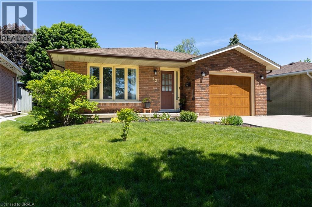 Brick exterior featuring a wood-finish garage door, a patterned paver driveway, a bay window with light-toned trim, and mature landscaping - 12 Spartan Drive, Brantford, ON - Outdoor