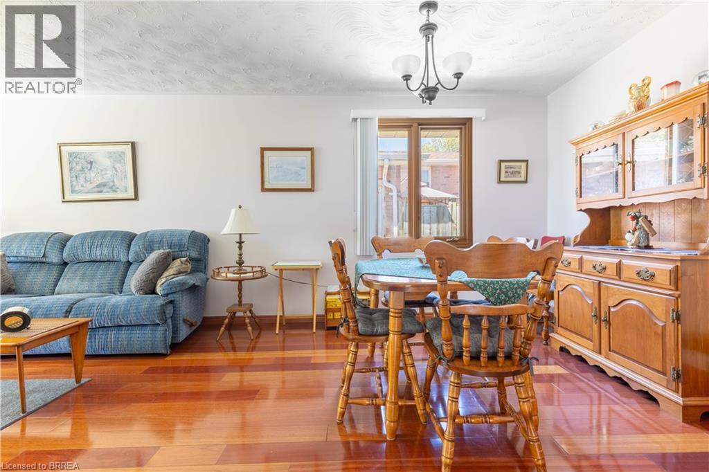 Open-concept living and dining area featuring wood-finish flooring, a contemporary chandelier, light-toned wall paint, and a window with a garden view - 12 Spartan Drive, Brantford, ON - Indoor