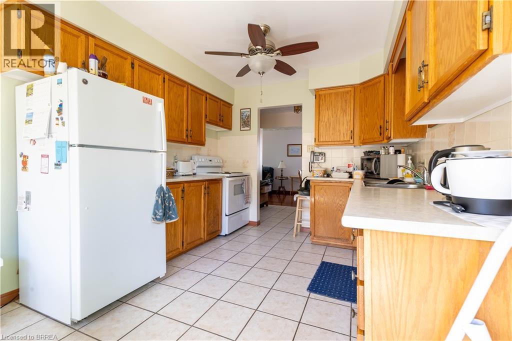 Kitchen featuring wood cabinetry, white appliances, white tile flooring, light countertops, and a ceiling fan with light fixture - 12 Spartan Drive, Brantford, ON - Indoor Photo Showing Kitchen
