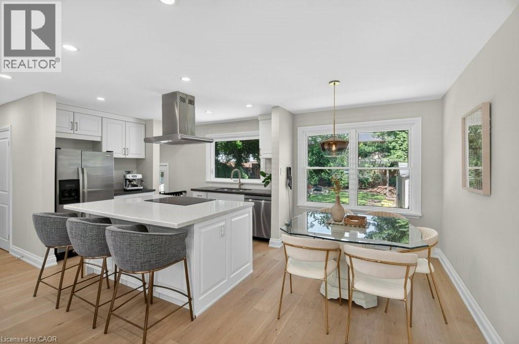 Open-concept kitchen and dining area featuring light wood-finish flooring, recessed lighting, white perimeter cabinetry, and a central island with countertop seating - 603 Cornick Drive, Burlington, ON