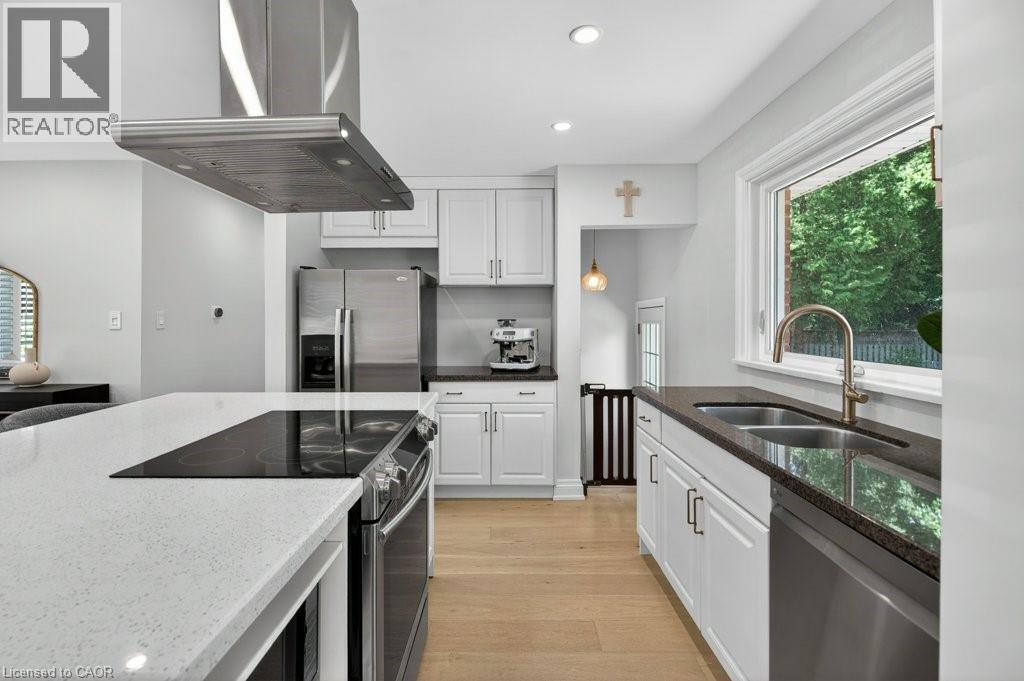 Kitchen featuring light wood-finish flooring, white cabinetry, stainless steel appliances, and a central island with a built-in cooktop and light-toned countertop - 603 Cornick Drive, Burlington, ON