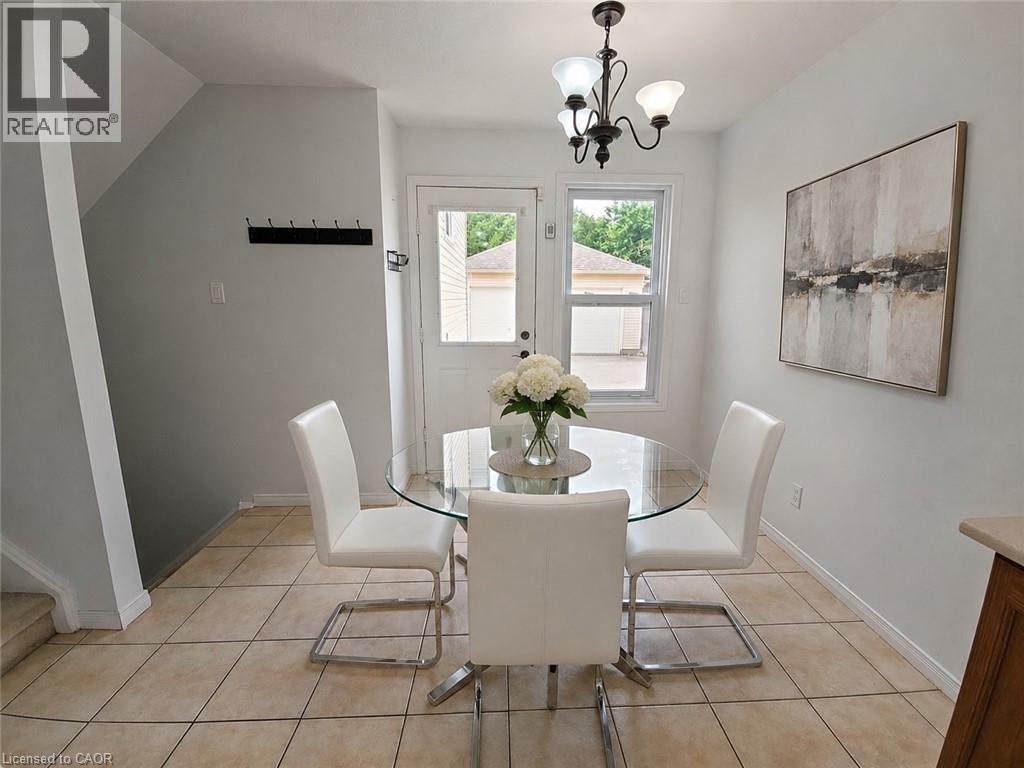 Tiled flooring throughout, featuring a glass-paneled door, a window with exterior views, and a three-light chandelier - 390 Wake Robin Crescent, Kitchener, ON - Indoor Photo Showing Dining Room