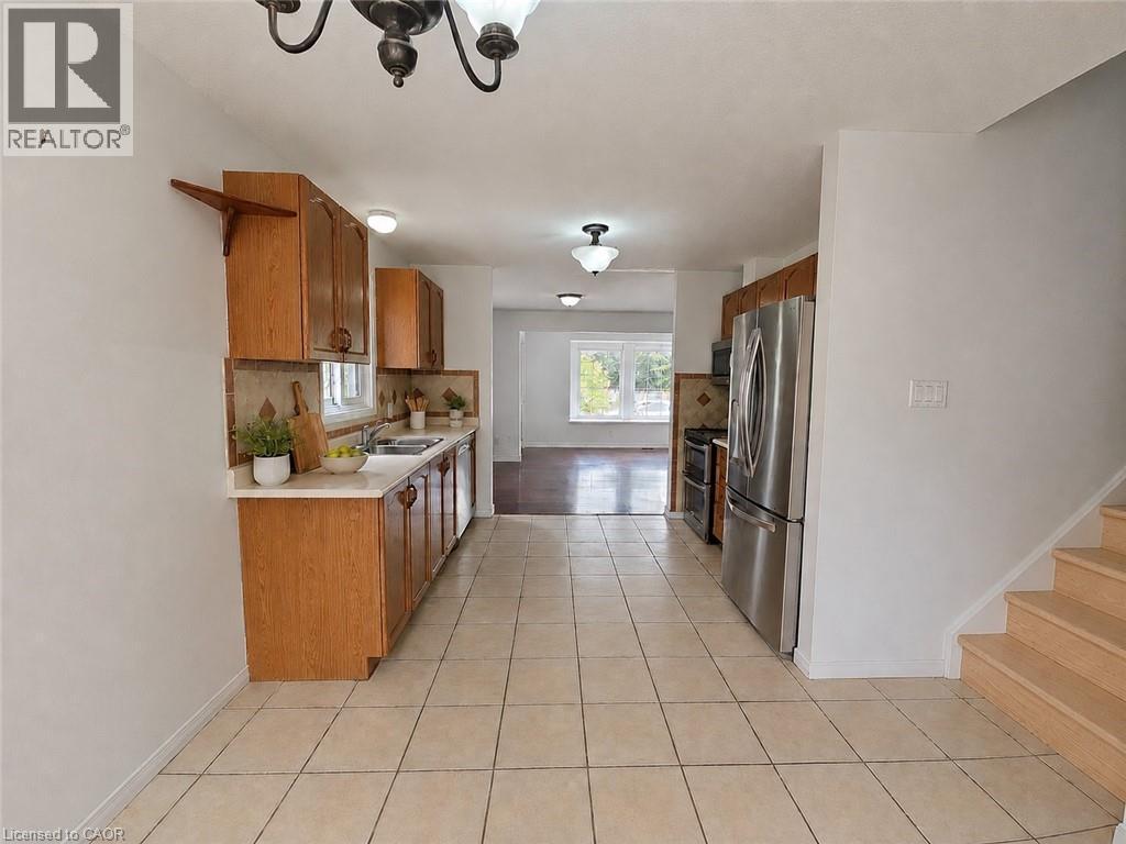 Kitchen featuring wood cabinetry, light-toned tiled flooring, stainless steel refrigerator, stainless steel range, and a tiled backsplash - 390 Wake Robin Crescent, Kitchener, ON - Indoor Photo Showing Kitchen With Double Sink
